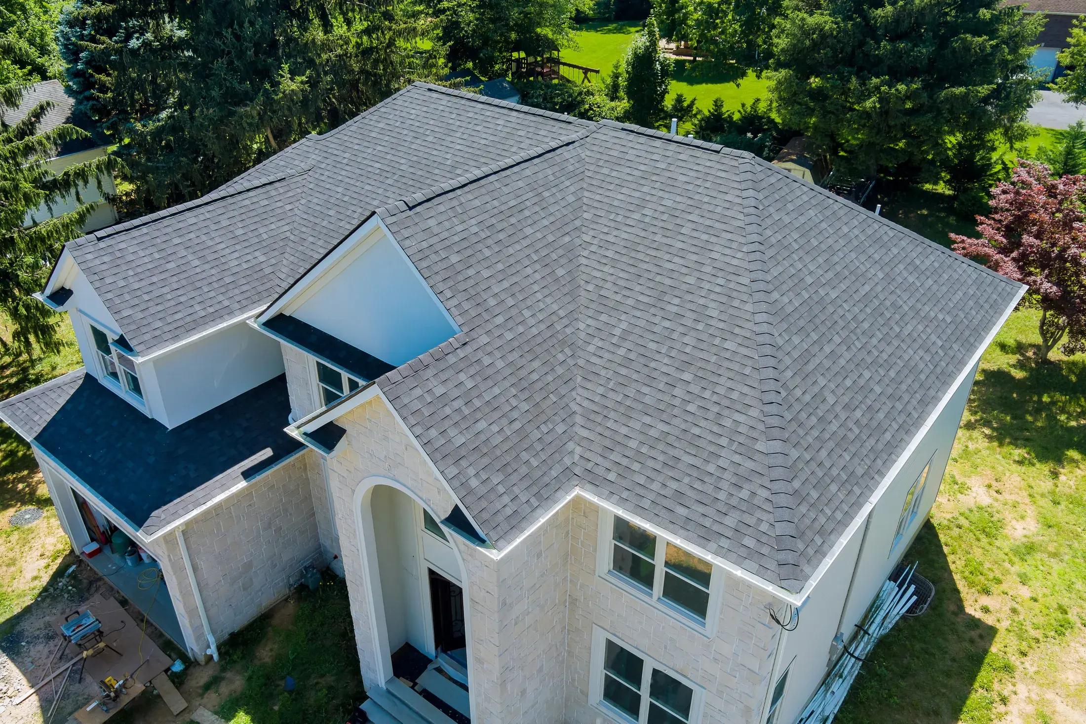 Aerial view of a two-story house with a newly installed gray asphalt shingle roof, showing multiple roof planes, valleys, and a dormer
