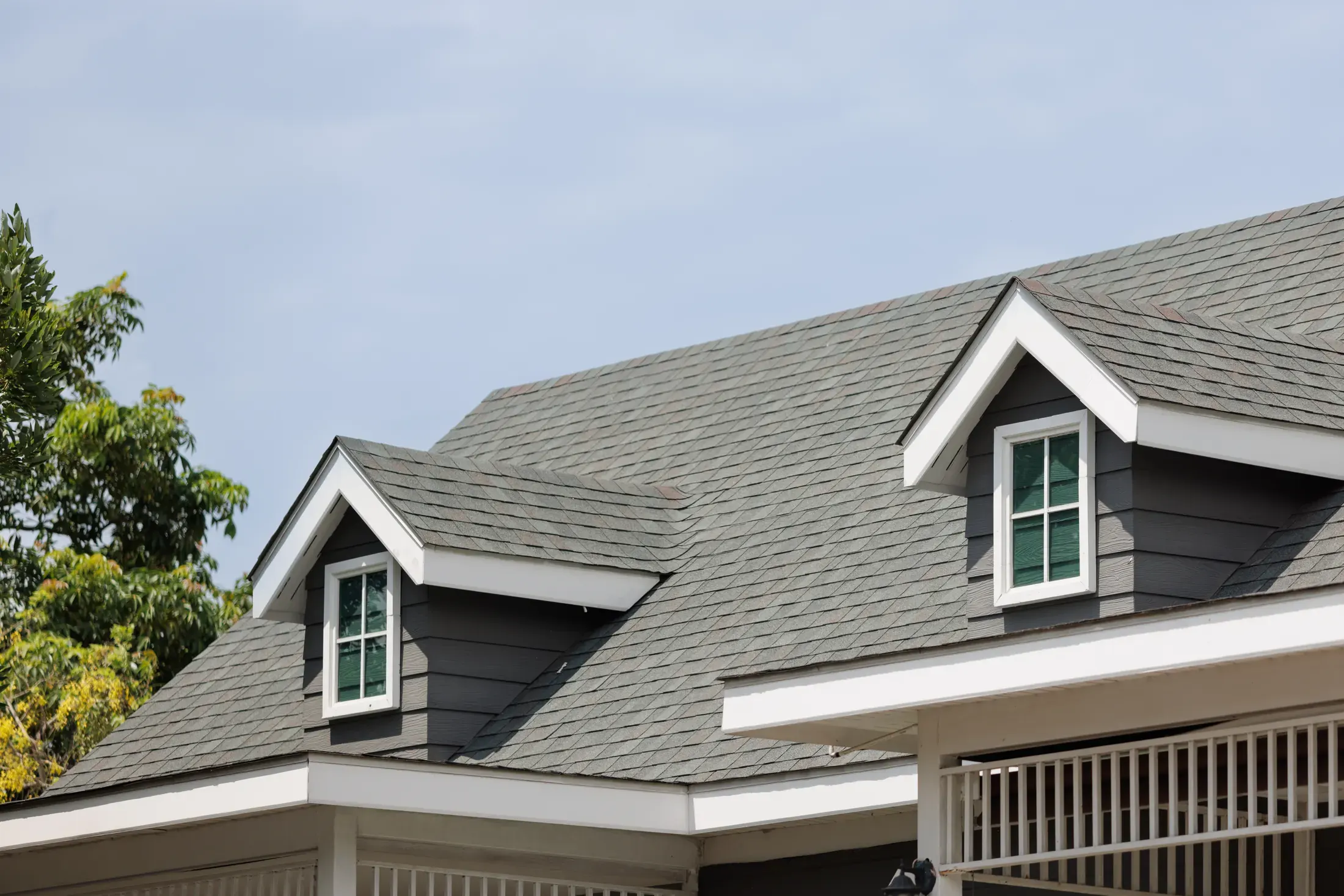 Gray architectural asphalt shingle roof with two gabled dormer windows on a residential home under a clear sky